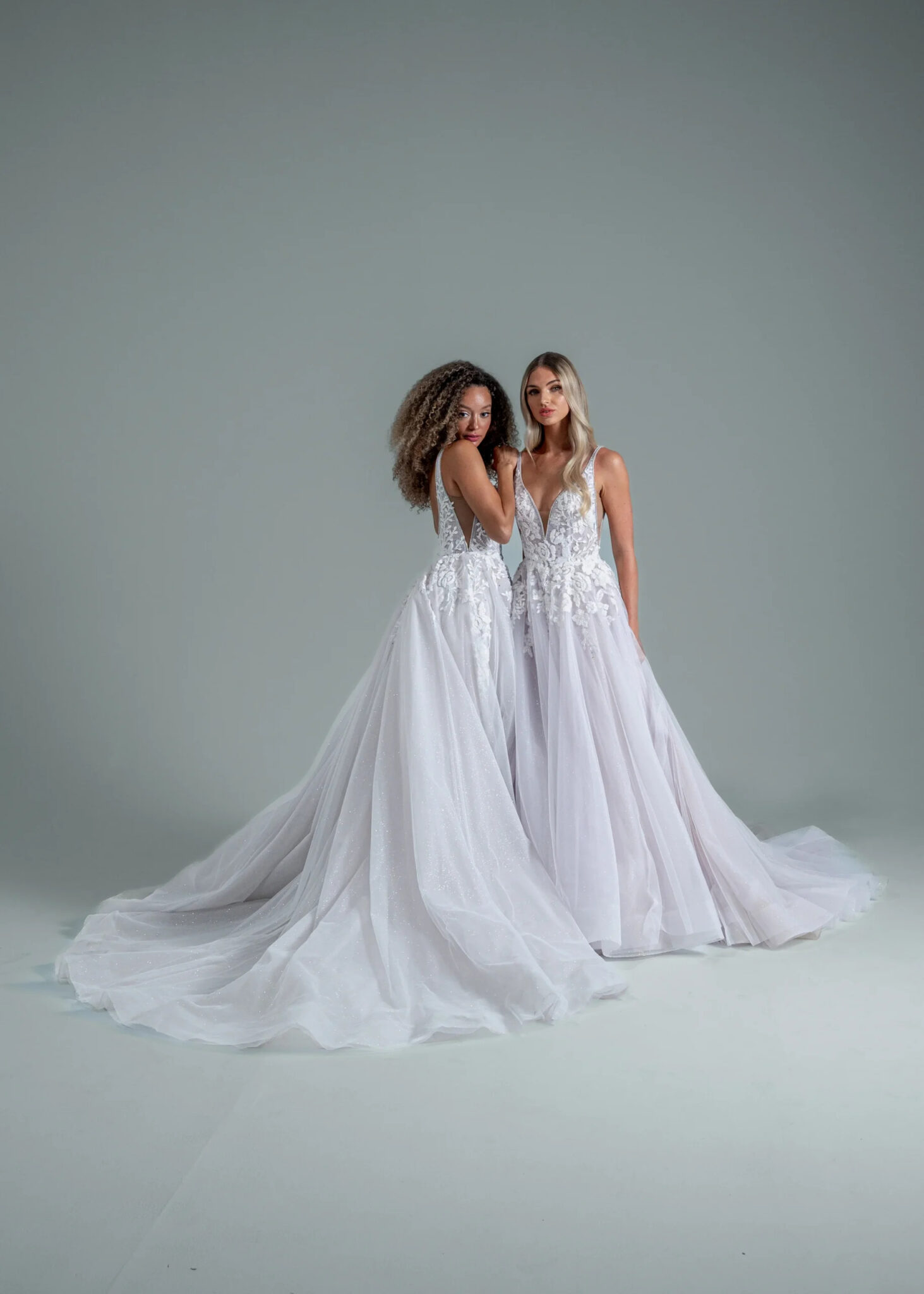 Two ladies wearing white wedding dresses with lace bodice and tulle skirt.
