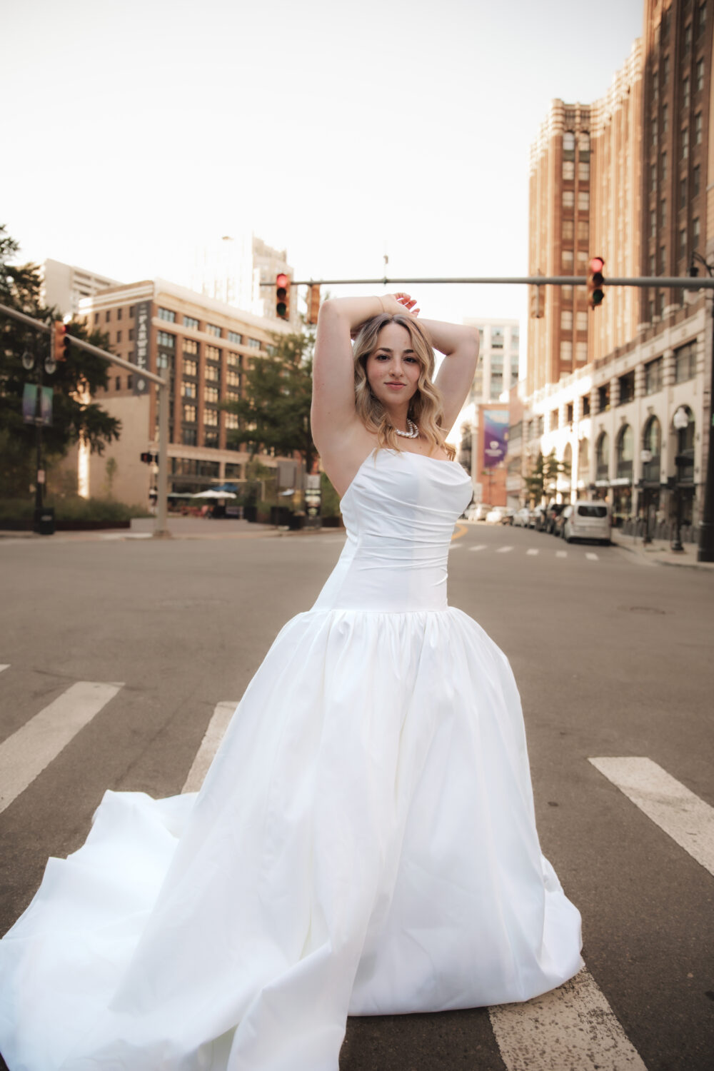 A bride poses confidently in the middle of a city street wearing a strapless ballgown wedding dress with a full skirt.