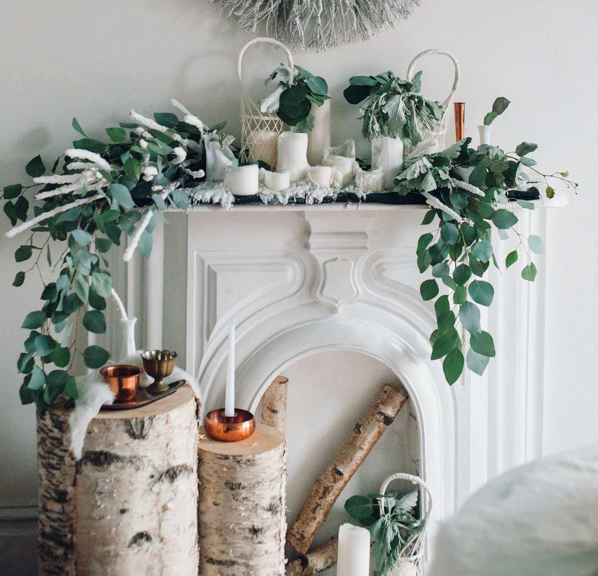 A winter-themed fireplace decorated with birch logs, white candles, and greenery arranged for a cozy wedding ambiance.
