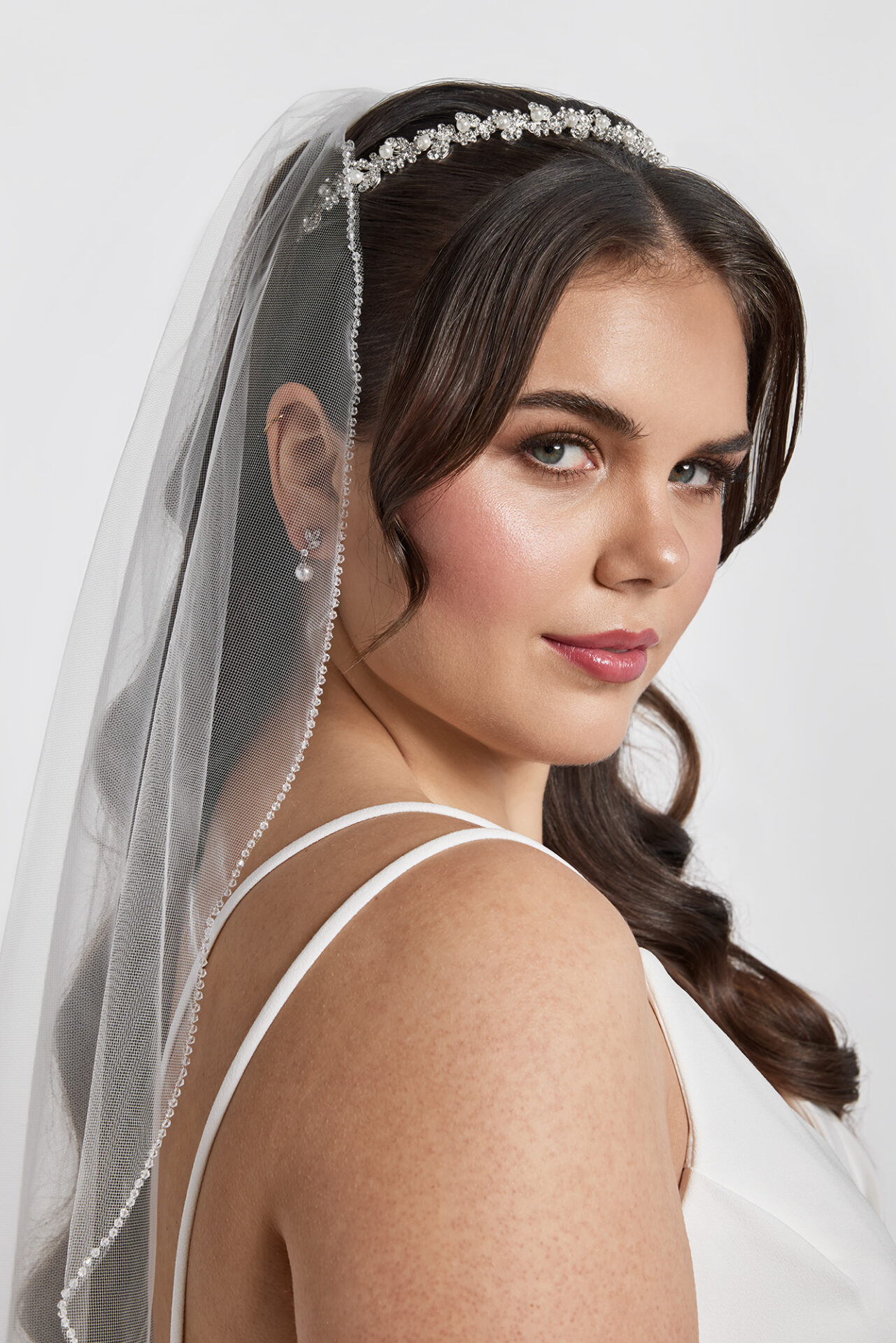 Bridal portrait of a woman with long wavy hair and veil, wearing a white gown.