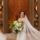 Bride standing in front of wooden chapel doors with her veil blowing behind her.