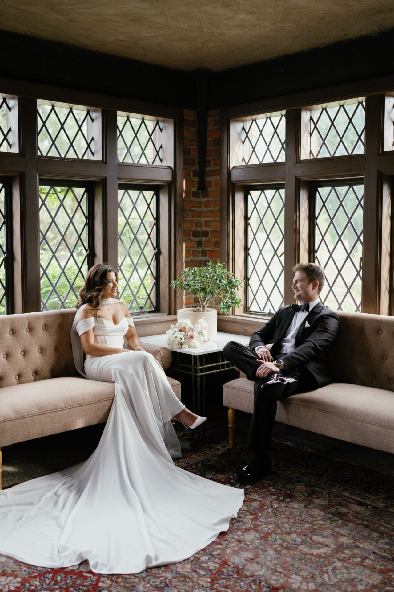 Bride in a fitted gown and groom sitting on a vintage sofa inside a historic venue.