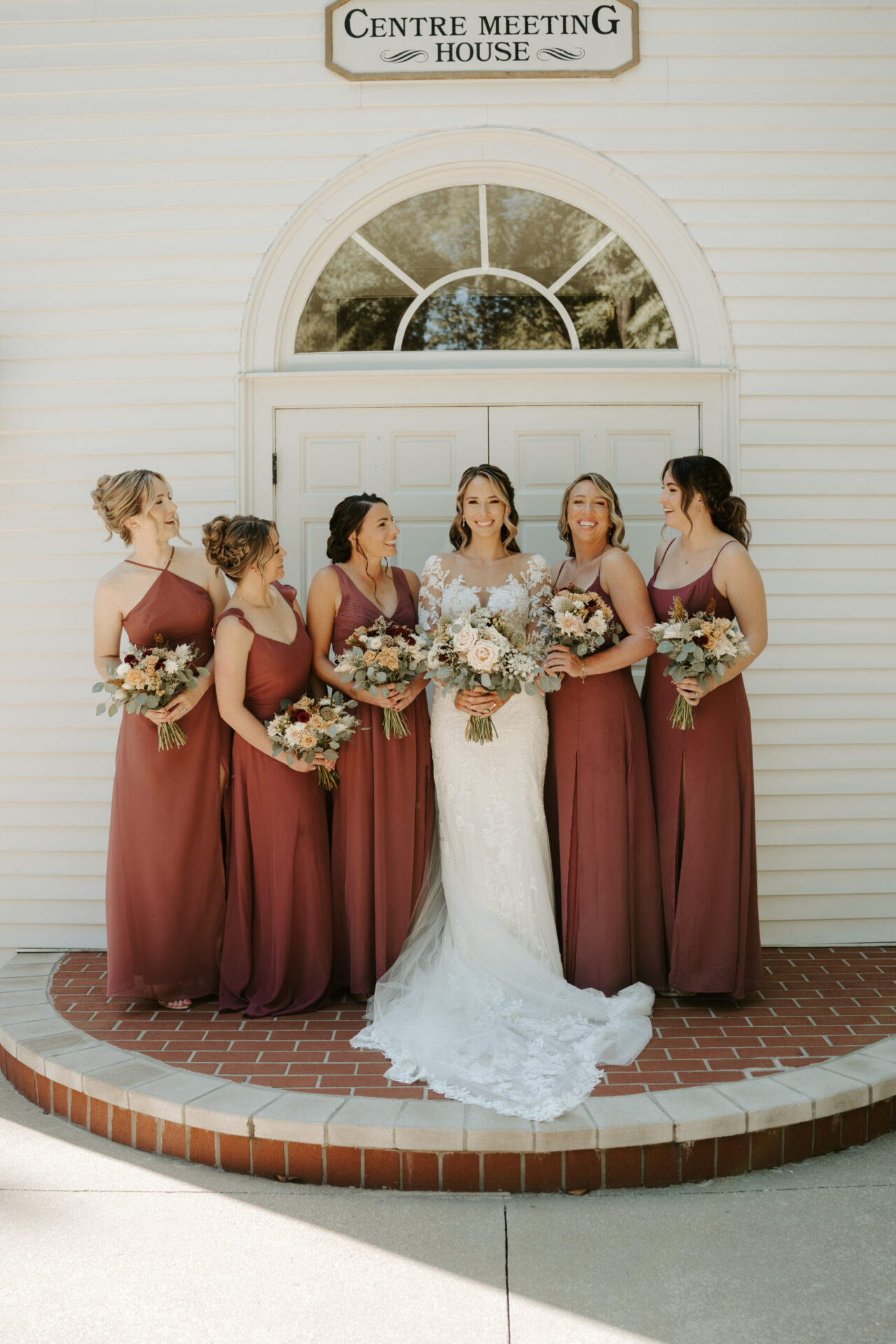 Bride with bridesmaids in matching dresses standing in front of a white chapel entrance.