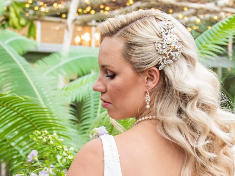Bride with wavy blonde hair styled half-up, looking down in a garden setting.