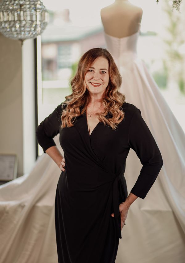 Bridal stylist or designer standing in front of a wedding dress in a studio.