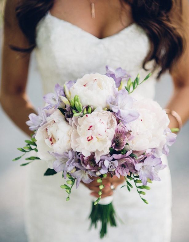 Bride holding a pastel pink and white bouquet close to her dress.