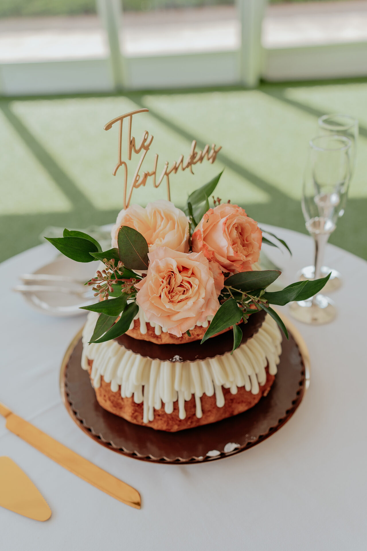 Small wedding cake decorated with peach roses and calligraphy topper.