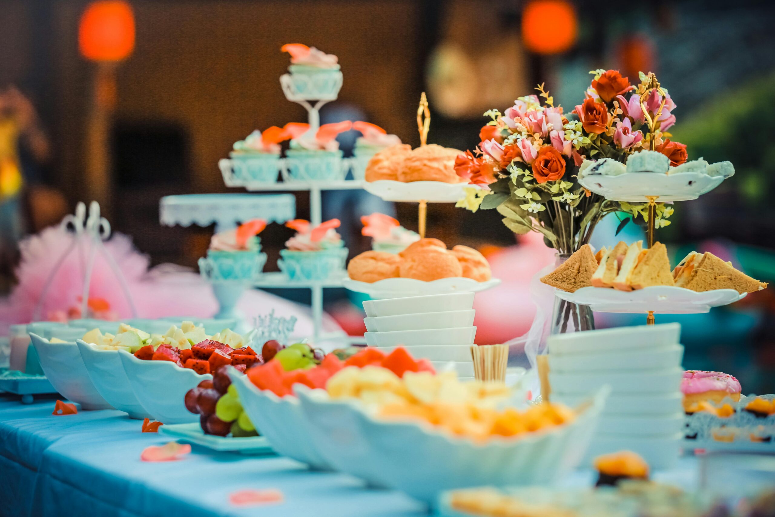 A colorful spring wedding dessert table with cupcakes, pastries, and floral décor arranged under warm ambient lighting.