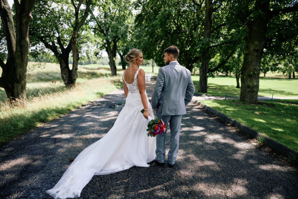 Bride and groom holding hands while walking down a tree-lined road.