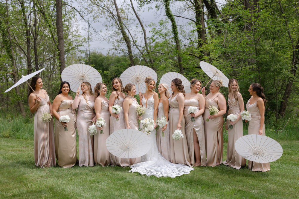 Bride with a group of bridesmaids holding parasols in an outdoor garden.