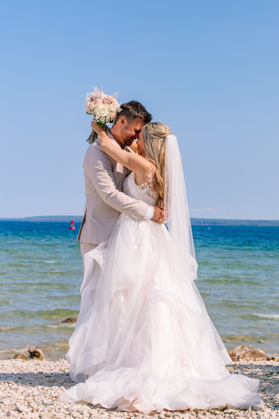 Bride and groom embracing on a beach with the ocean in the background.