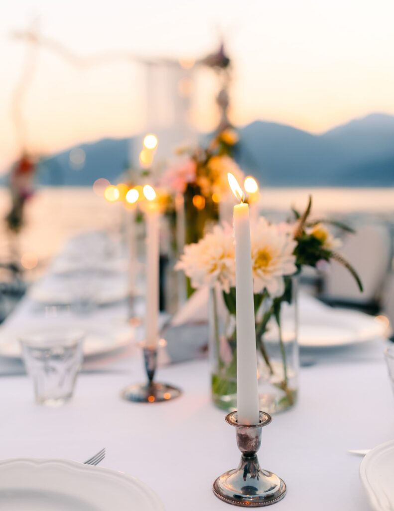Romantic wedding table at sunset with candles, glassware, and soft lighting.