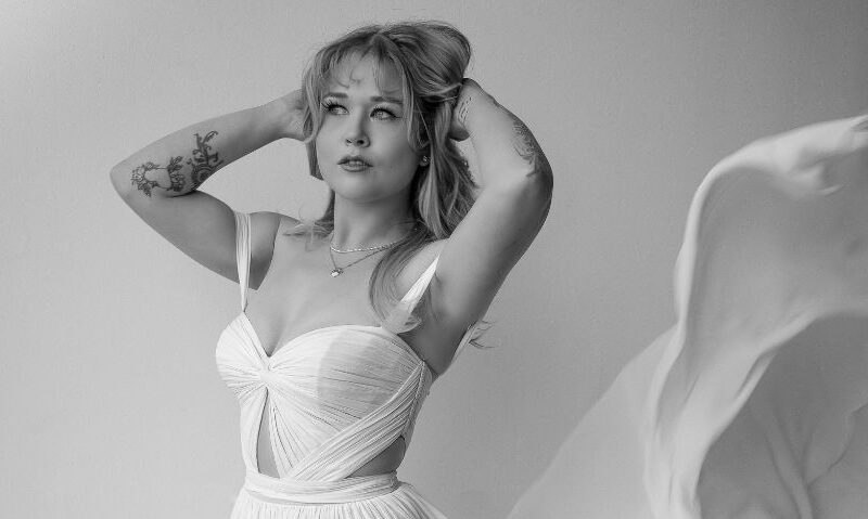 A bride in a flowing gown lifts her arms as the fabric billows around her in a dramatic black and white portrait.