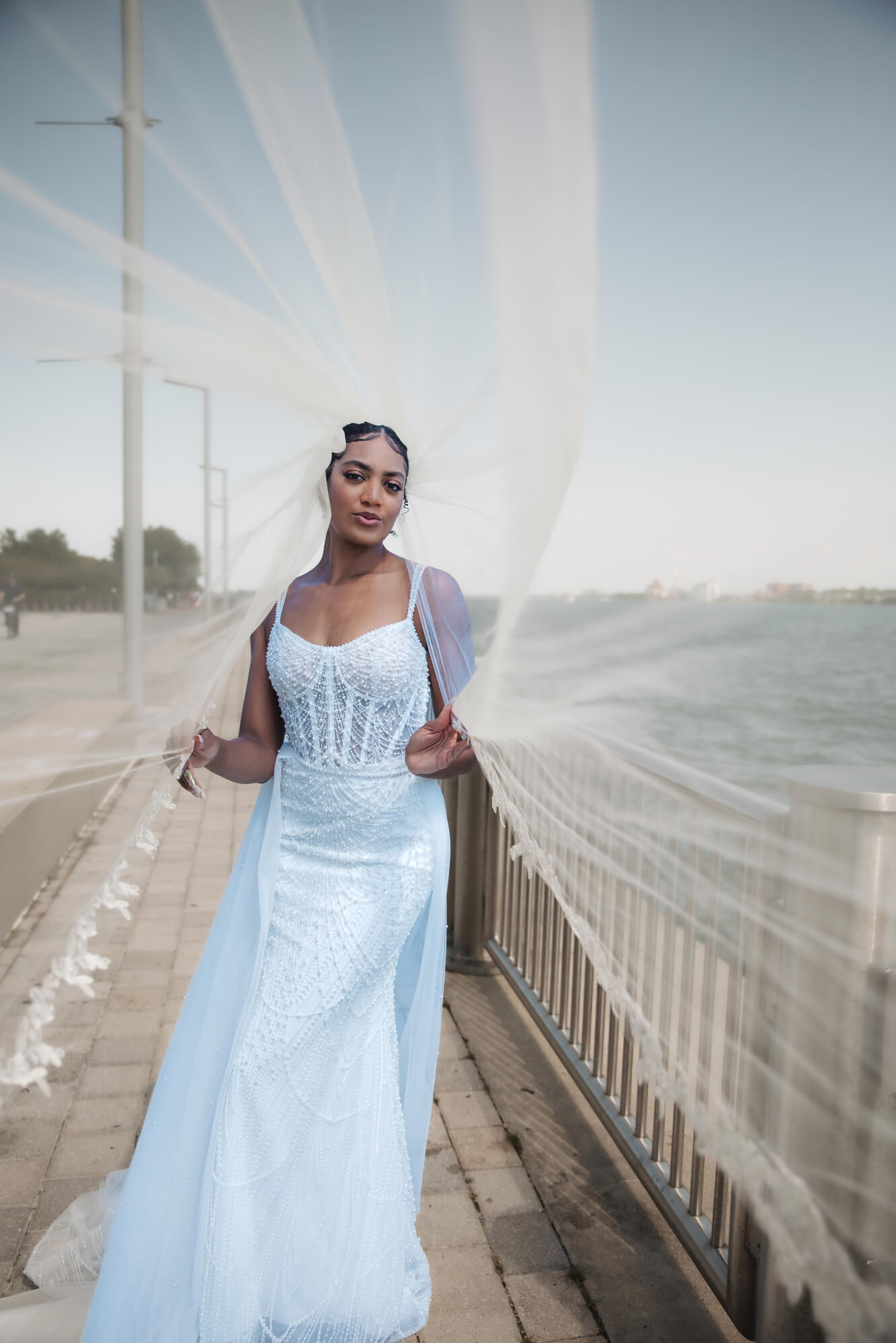 Bride standing outdoors on a bridge wearing a blue flowing wedding gown with a long train blowing in the wind.