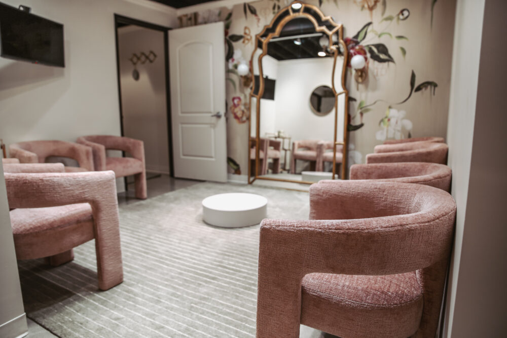 A bridal fitting area with pink upholstered chairs arranged around a circular platform in front of a large ornate mirror.