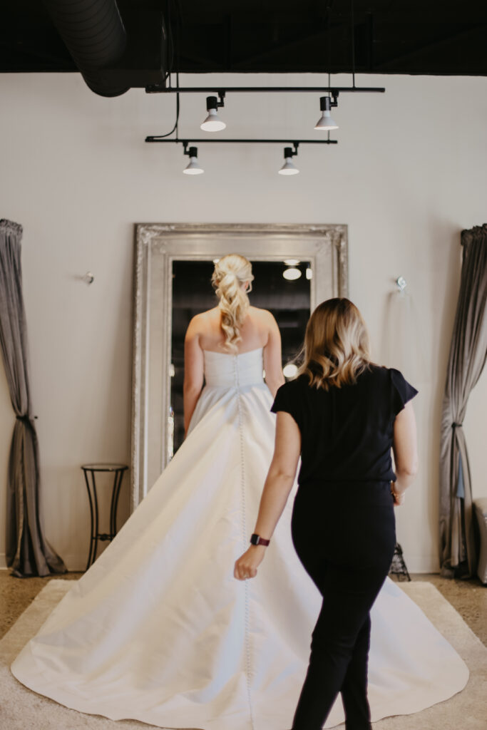 Bridal stylist adjusting the train of a wedding dress during a fitting inside a boutique.