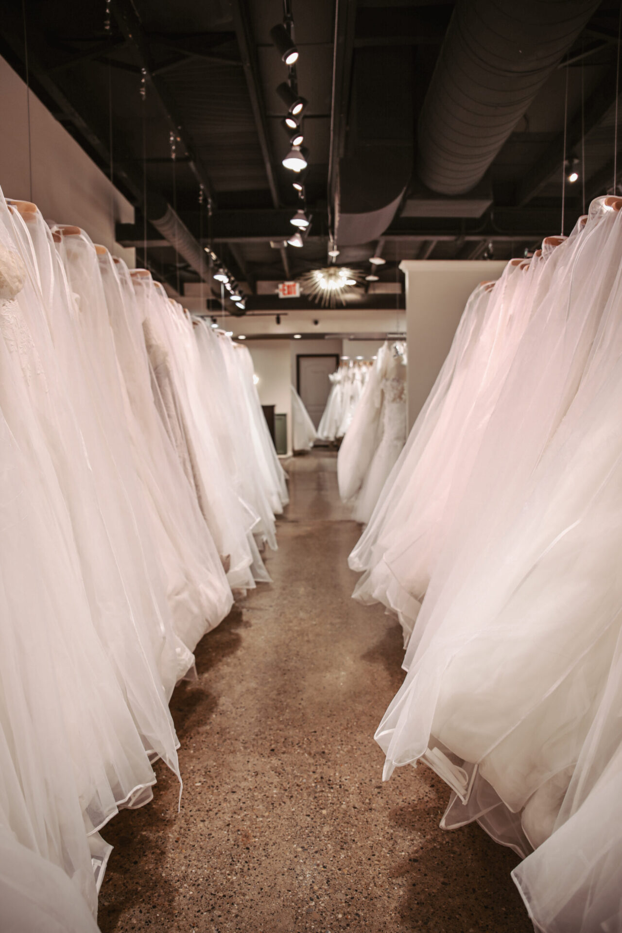 Rows of white wedding dresses hanging neatly inside a bridal boutique showroom.