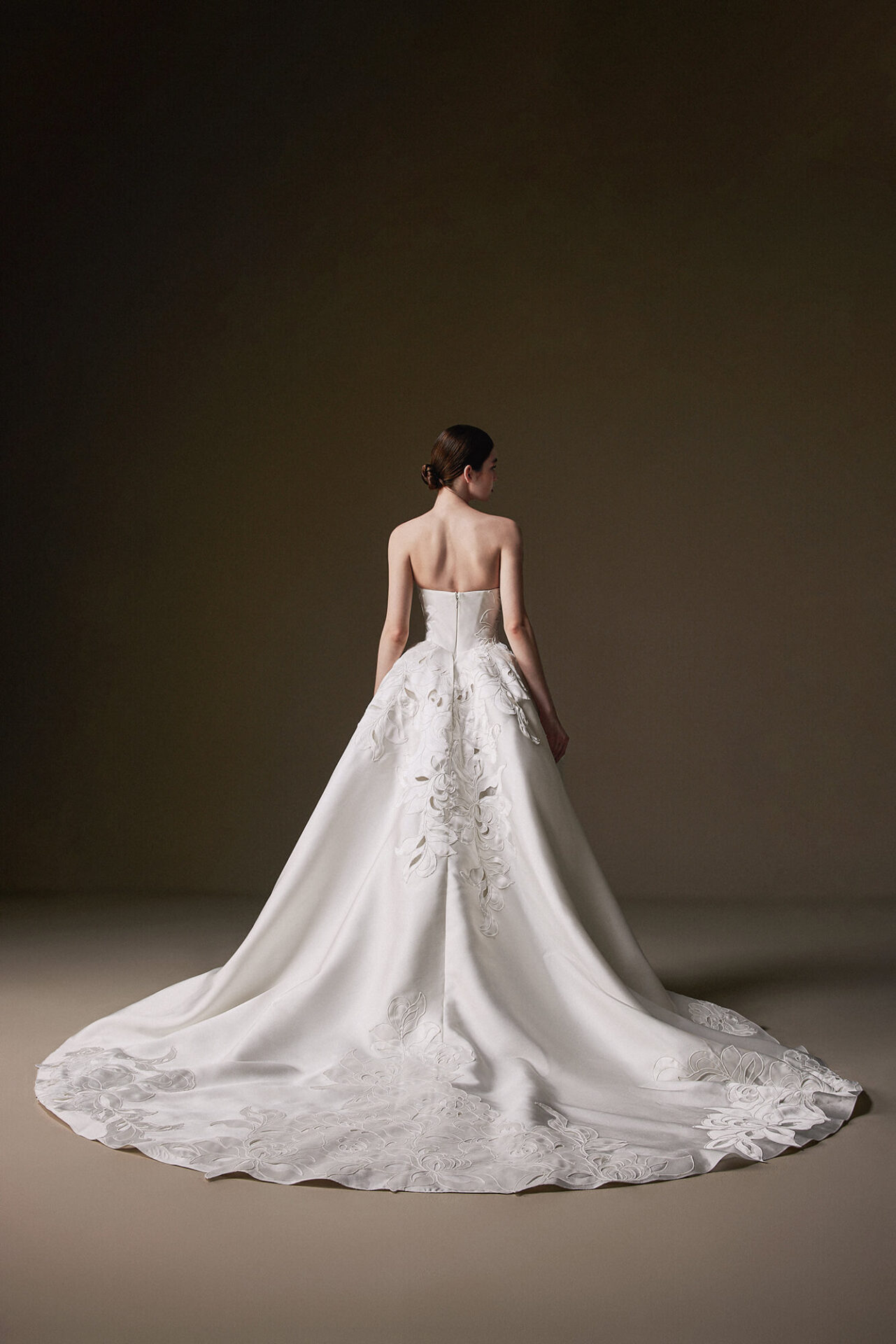 Bride in a dramatic backless wedding gown with a cathedral-length train standing in a studio setting.