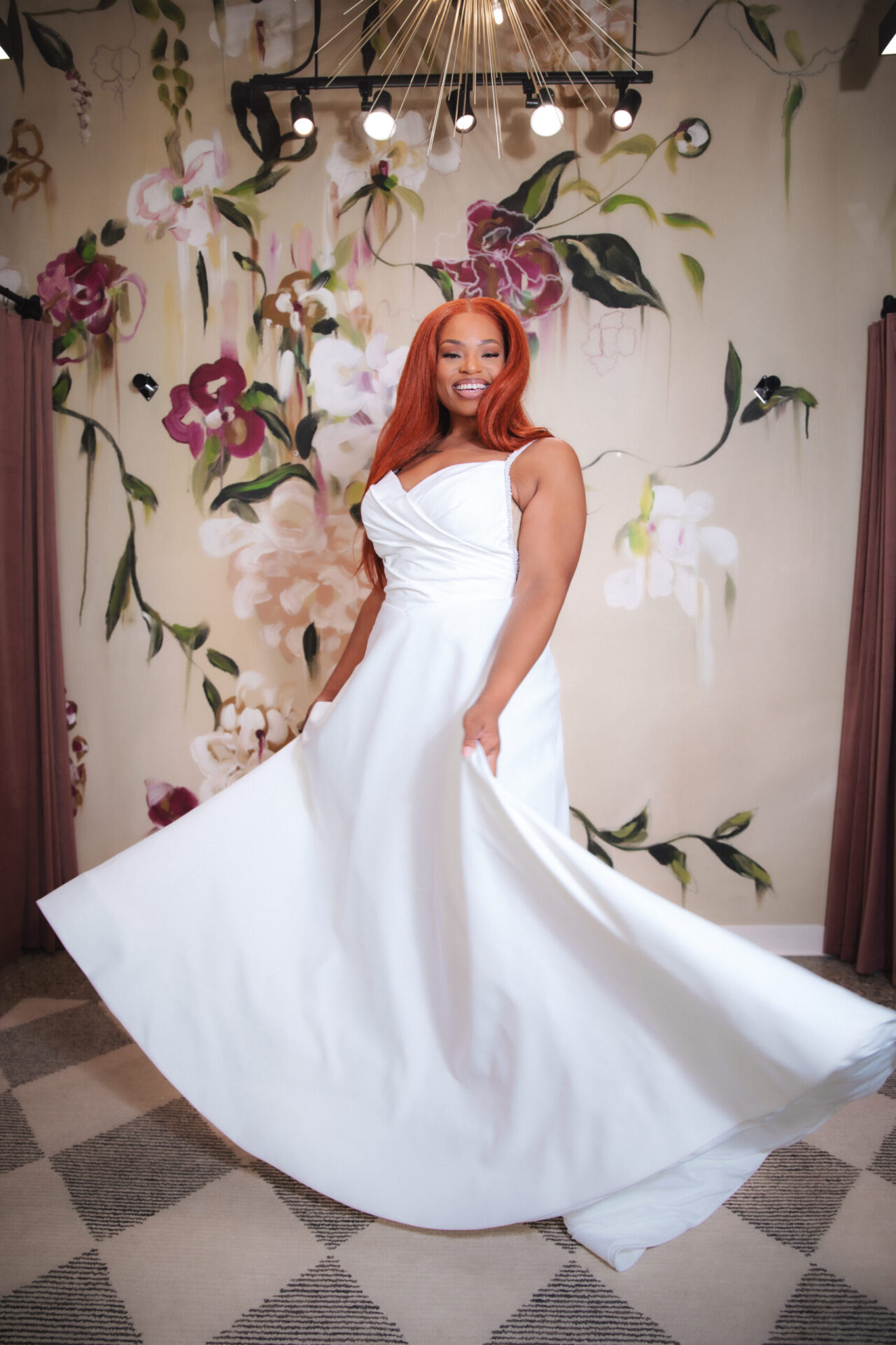 Bride twirling in a minimalist sleeveless wedding gown in front of a floral boutique backdrop.