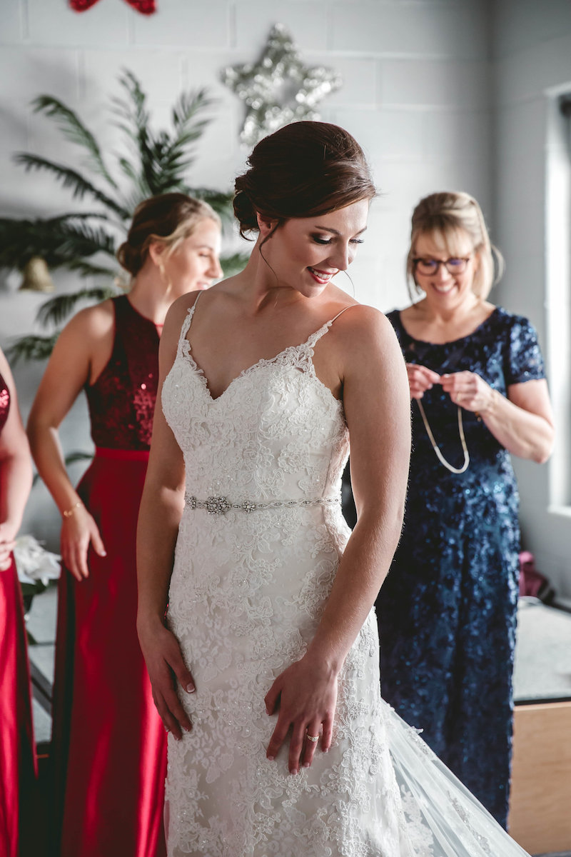 Bride wearing a lace V-neck gown being assisted by a stylist during a wedding dress fitting.