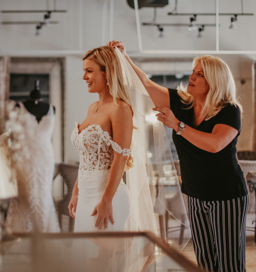 Bridal consultant assisting a bride during a wedding dress fitting in a boutique.