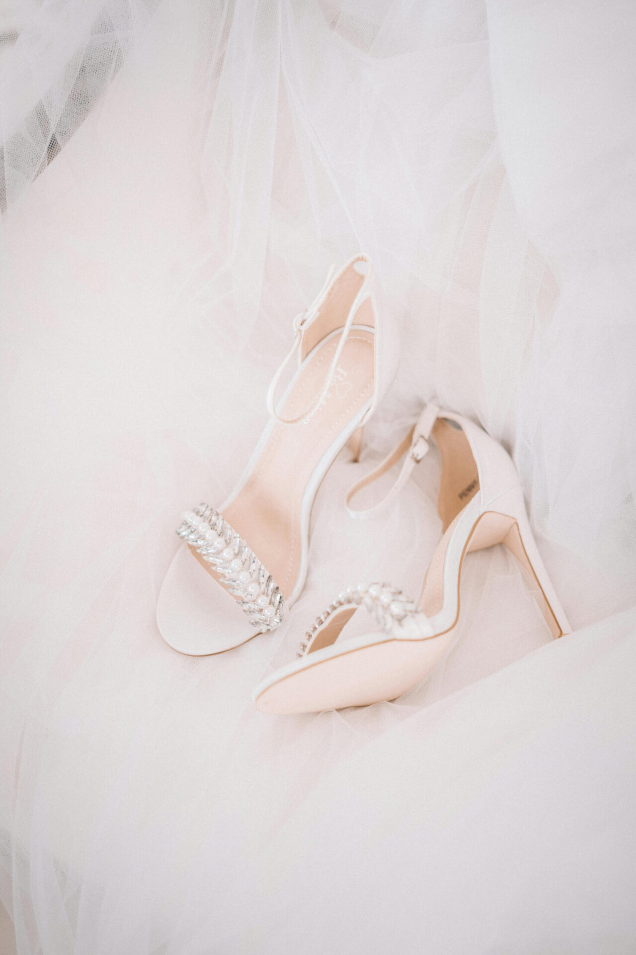 Flat-lay of bridal accessories, including heels, and a veil arranged on a soft white background.