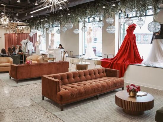 A spacious bridal boutique interior with velvet sofas, display gowns in the window, and groups of people seated during appointments.