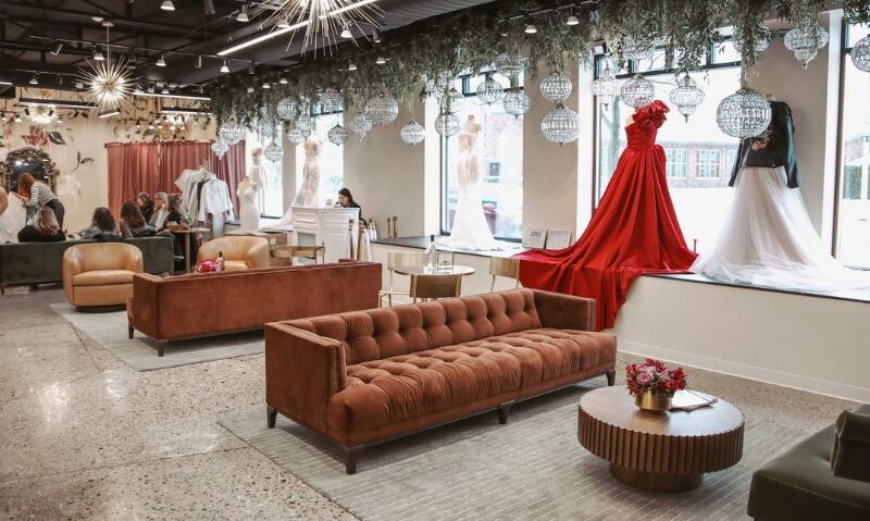 A spacious bridal boutique interior with velvet sofas, display gowns in the window, and groups of people seated during appointments.