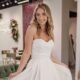 A bride in a strapless a-line wedding dress poses inside a bridal shop holding the skirt out to the sides.