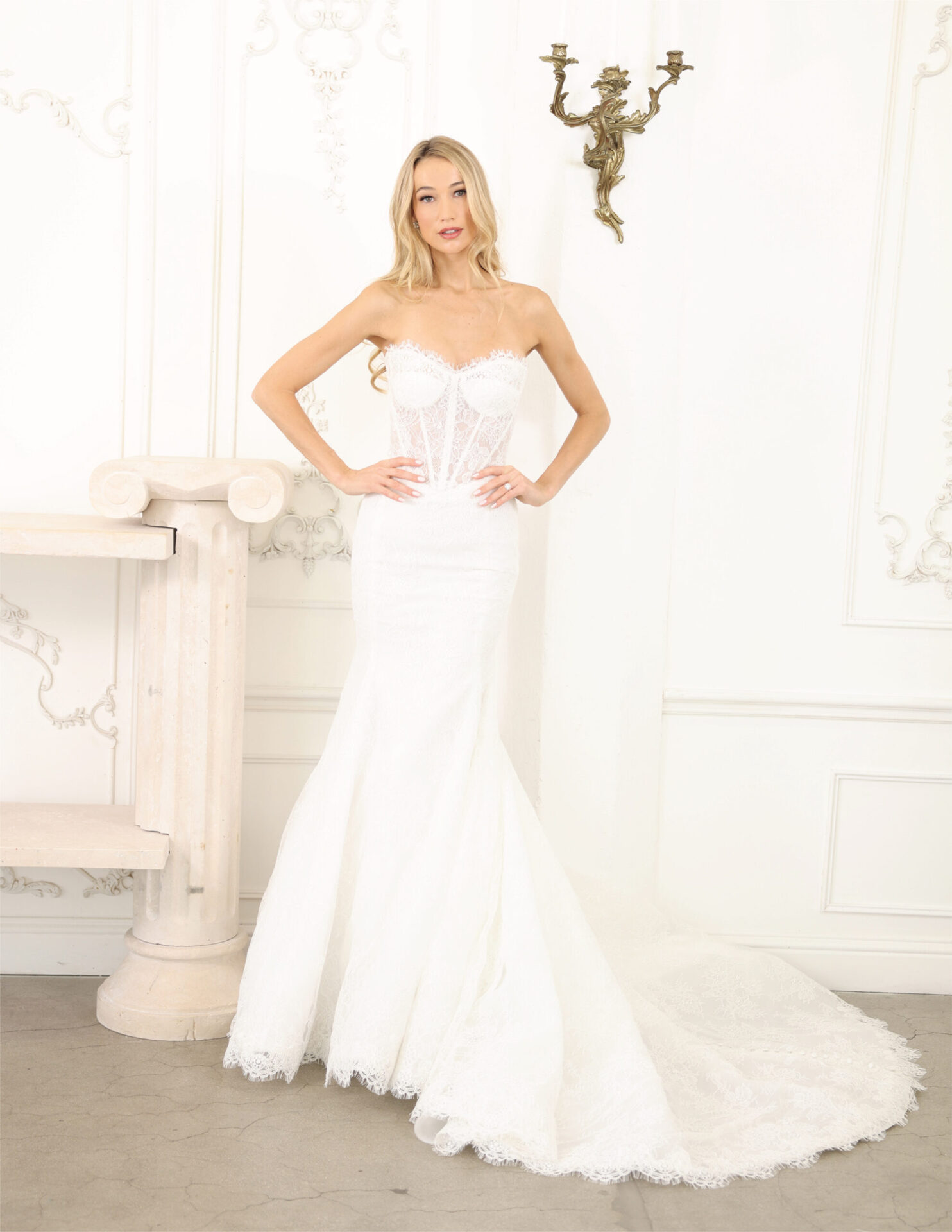 Bride in a fitted strapless couture gown with a subtle train, standing in a classic white room.