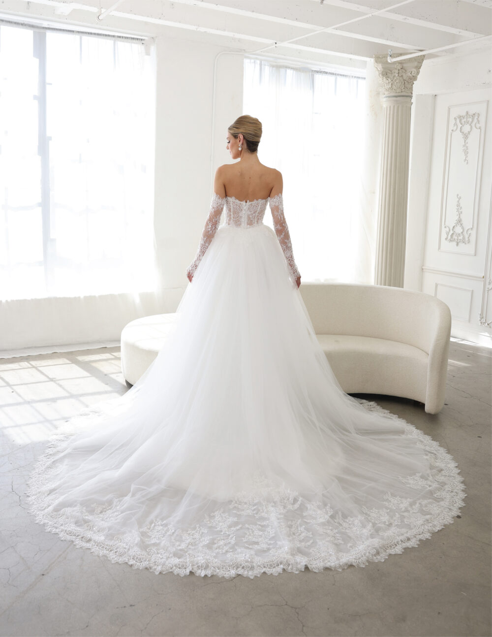 Back view of a bride in an off-the-shoulder gown with a lace-trimmed circular train.