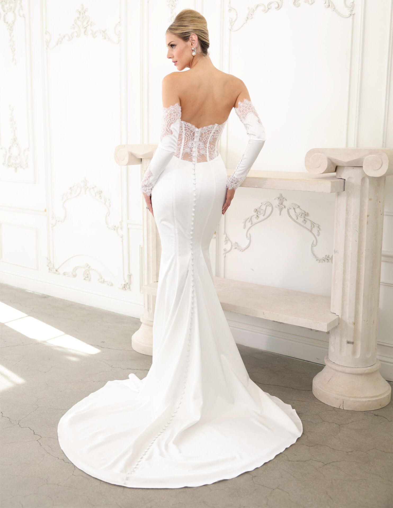 Back view of a bride in a fitted couture gown with sheer sleeves and a smooth train.