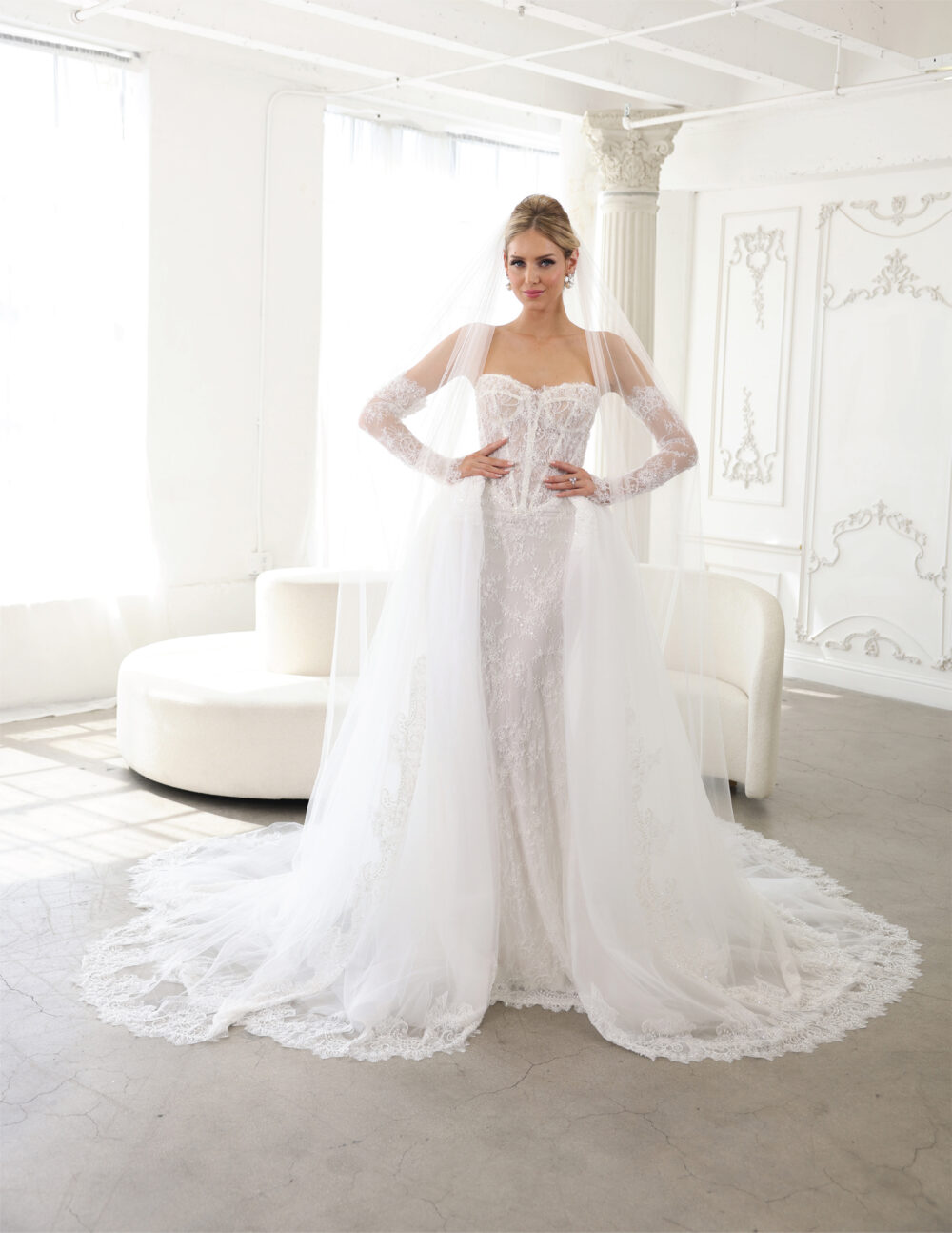 Bride in a strapless lace gown standing gracefully in a minimalist studio setting.