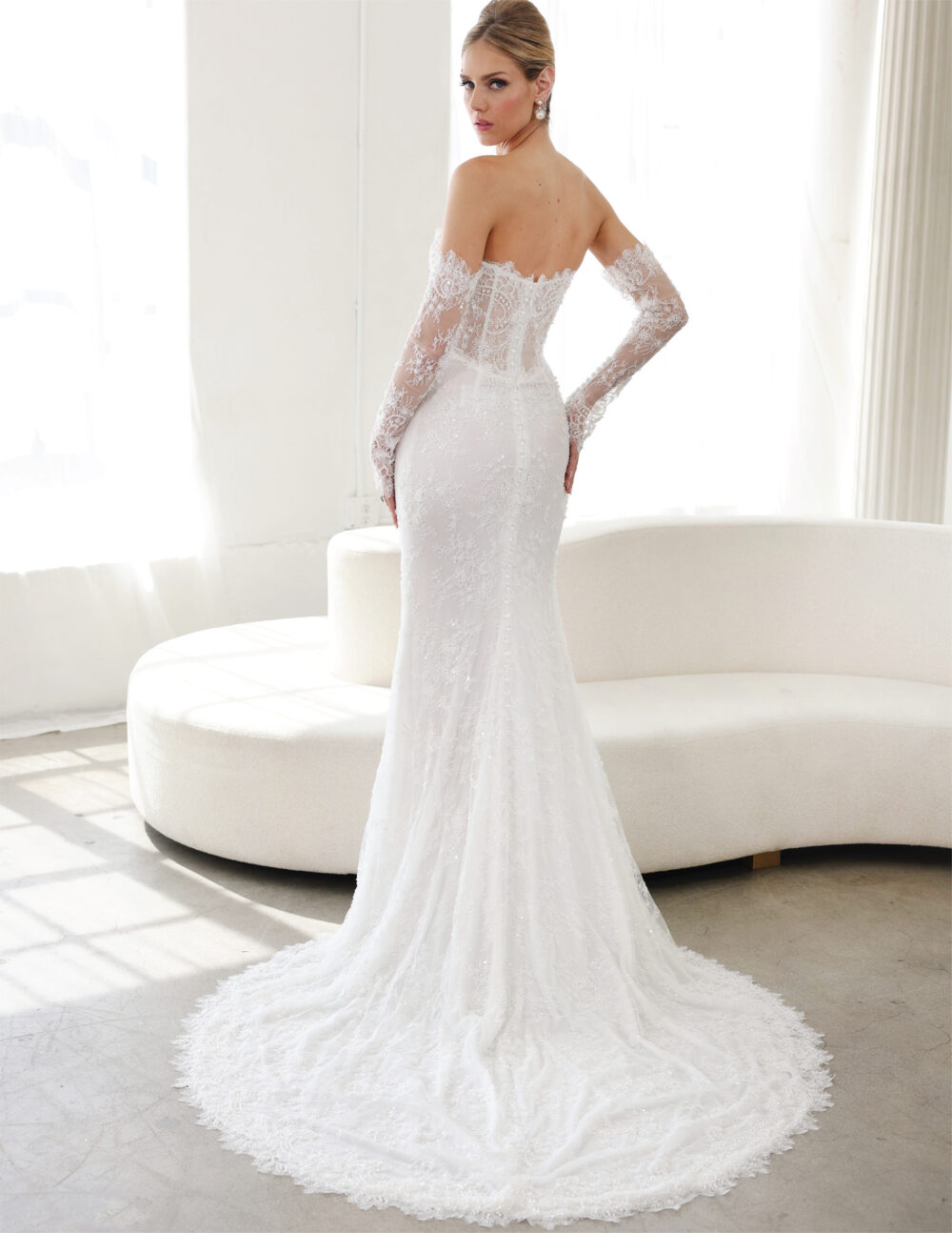 Back view of a bride in a fitted lace gown with sheer sleeves and a smooth train.