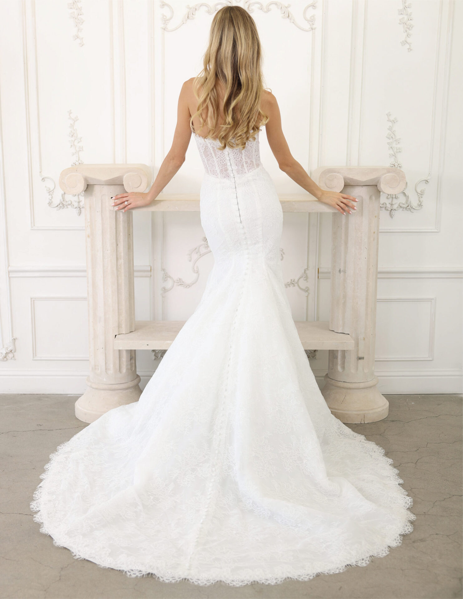 Back view of a bride in a fitted couture gown with lace detailing and a rounded train.