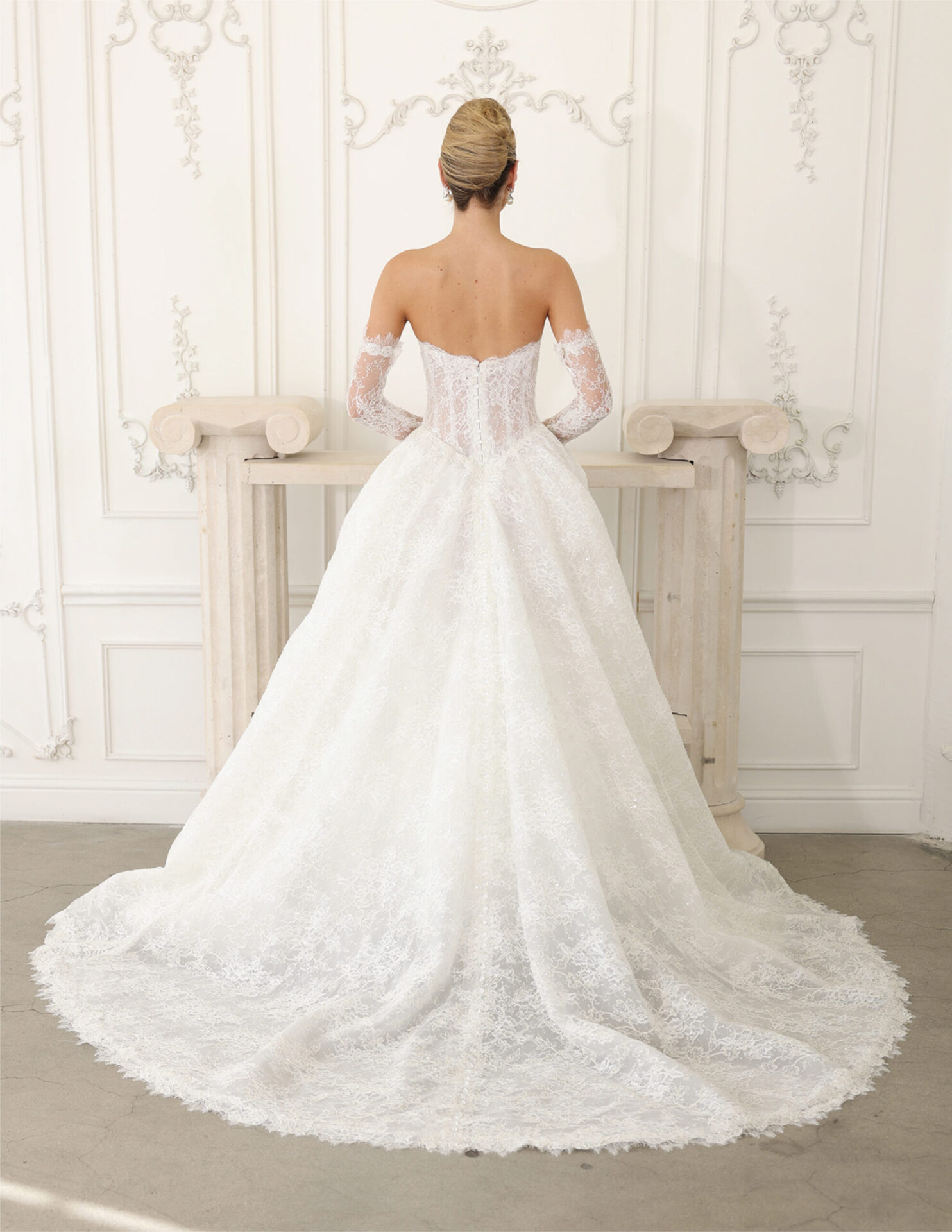 Back view of a bride in an off-the-shoulder lace couture gown with a dramatic circular train.