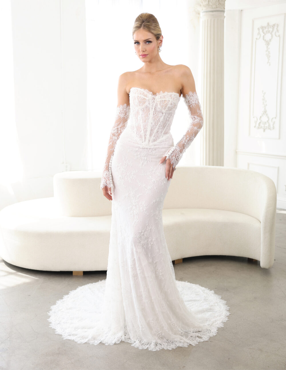 Bride in a fitted off-the-shoulder lace wedding gown standing in a bright white studio.