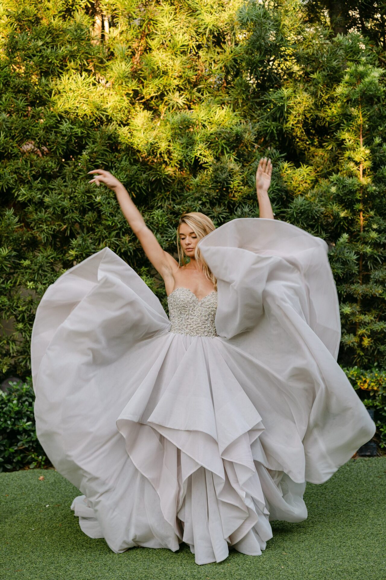 Bride in a voluminous white gown, tossing the skirt of her voluminous gown in a garden.