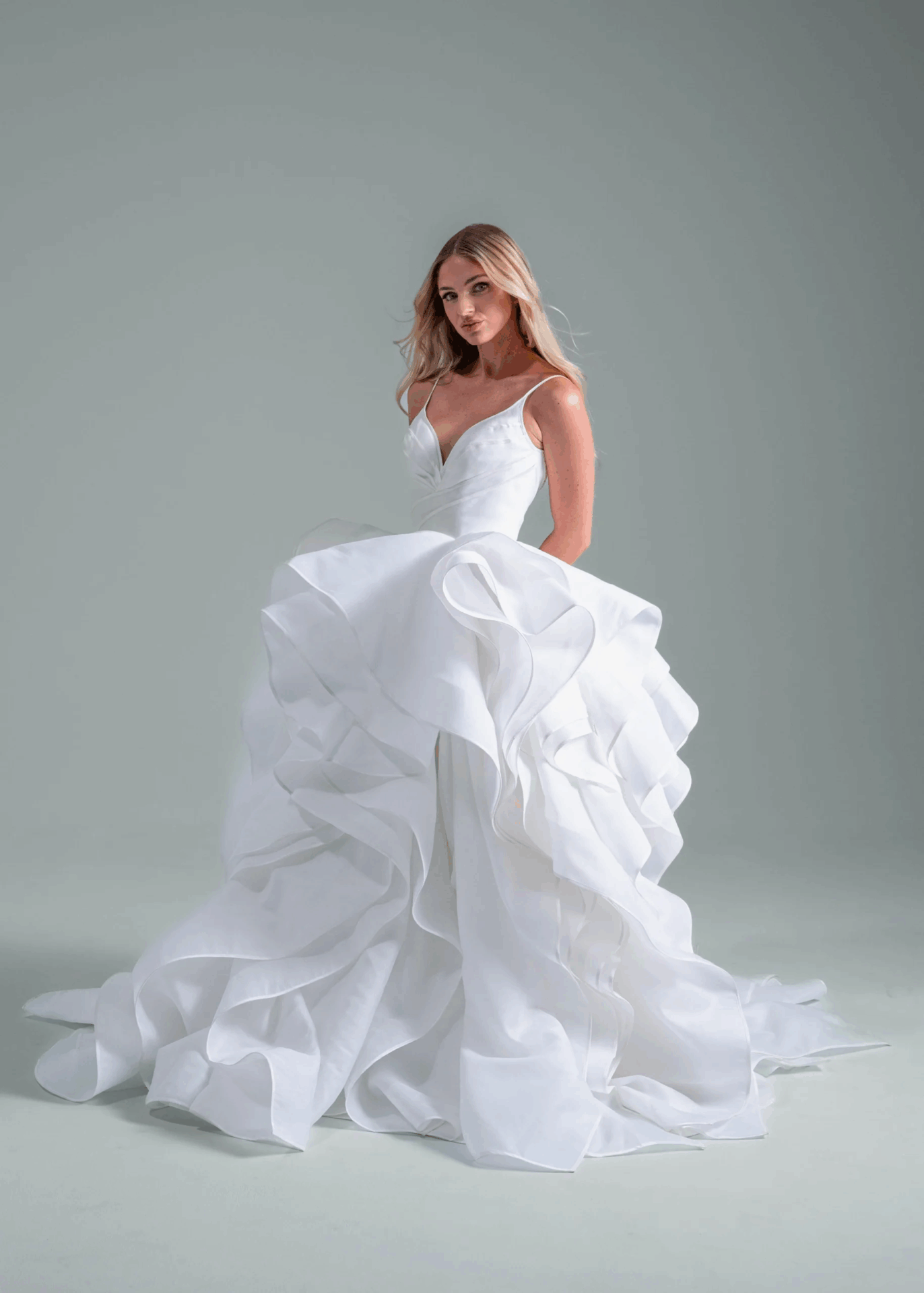 Bride in a layered wedding dress posing against a soft gray studio backdrop.