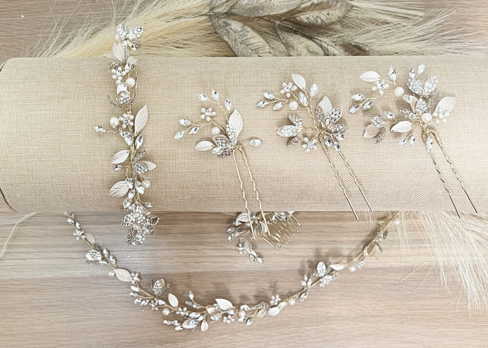 A set of crystal floral hairpins and a matching vine headpiece are displayed on a beige fabric roll.