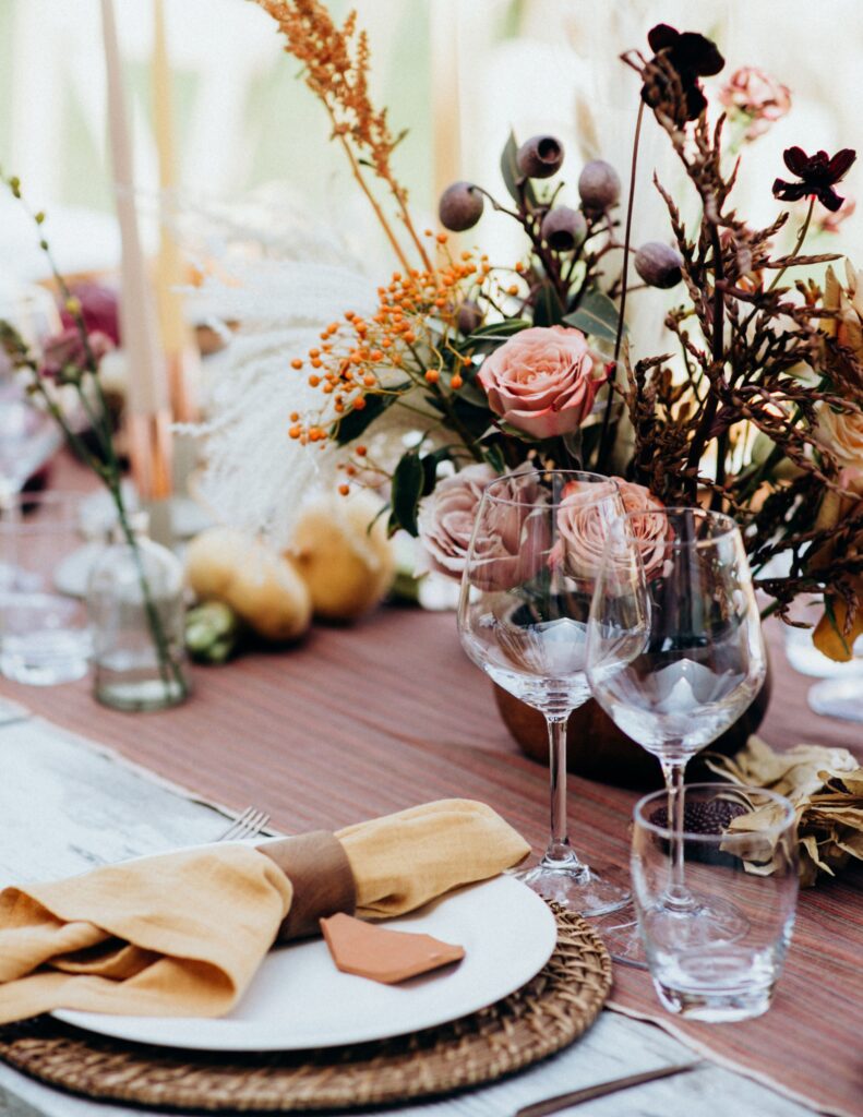 A close-up of a wedding reception table decorated with candles, fruit, greenery, and neatly arranged wine glasses and napkins.