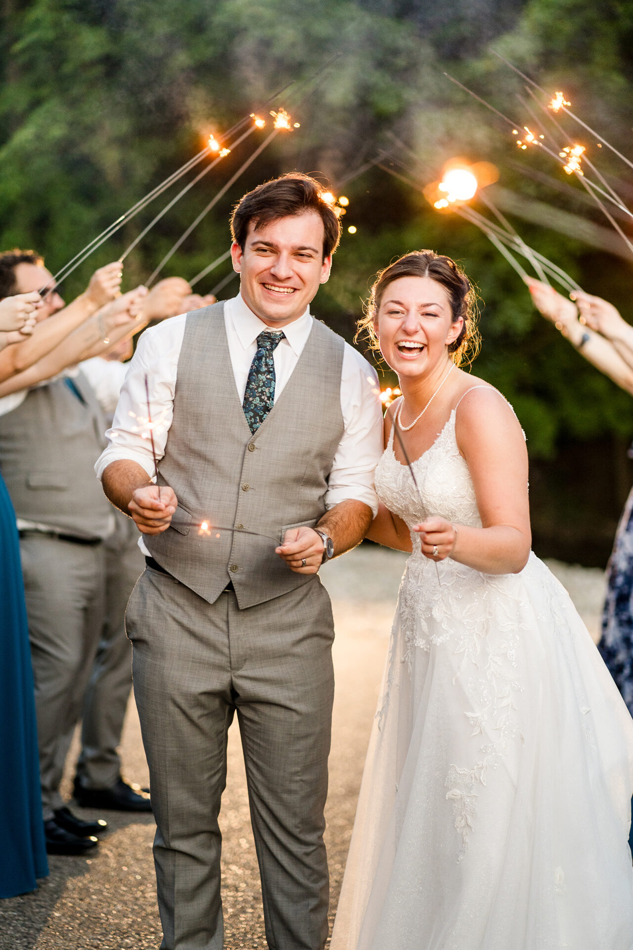 Bride and groom standing together at night while guests hold sparklers around them in celebration.