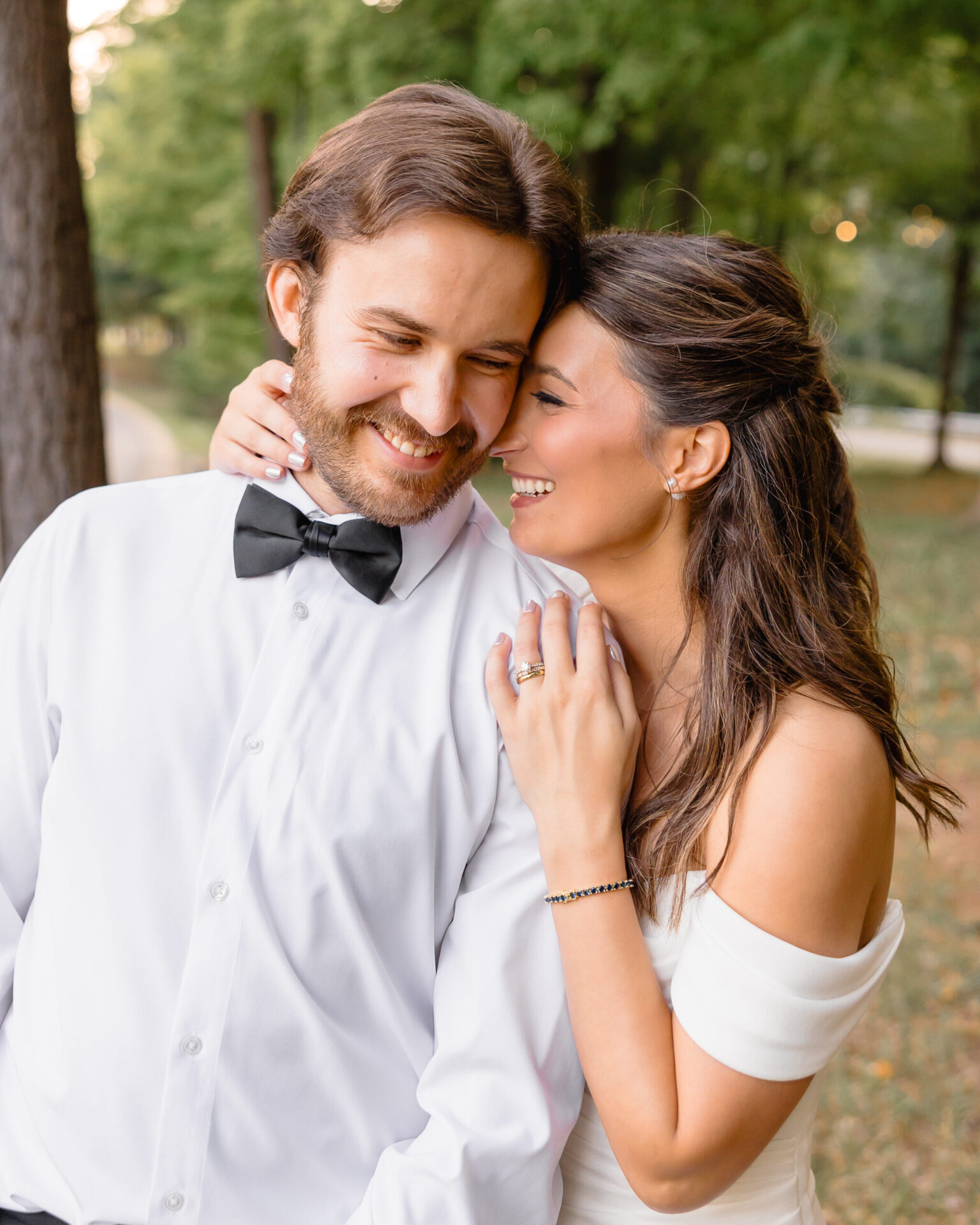 Bride and groom standing close together outdoors, smiling and laughing with their arms wrapped around each other.