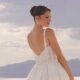 Close-up of a bride in a lace wedding dress with thin straps looking over her shoulder in a bright desert setting.