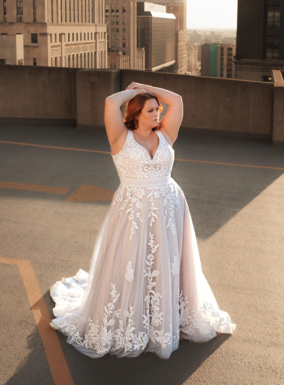 A woman in a long white wedding dress stands on a rooftop with city buildings in the background.