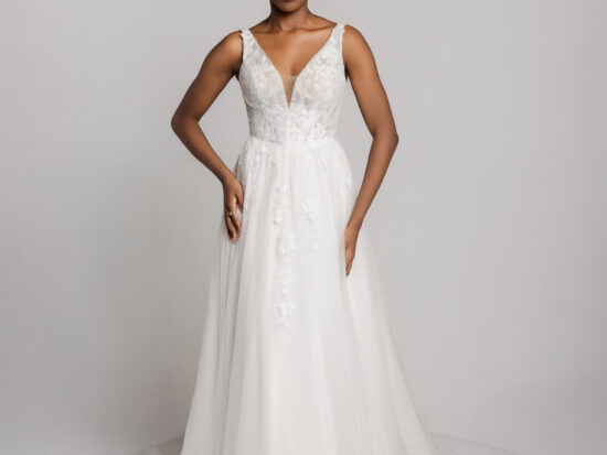 Bride in a sleeveless white wedding gown with a V-neckline and fitted bodice, standing with hands on hips.