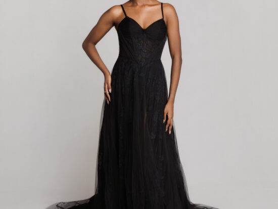 Bride wearing a black wedding gown with thin straps, a fitted bodice, and a sheer tulle skirt with a long train, standing against a neutral background.