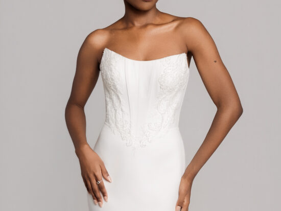 Close-up of a bride in a strapless fitted white gown with a structured bodice, posing against a neutral backdrop.
