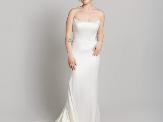Bride wearing a strapless fitted white wedding gown with a straight neckline and slight train, posing against a neutral background.