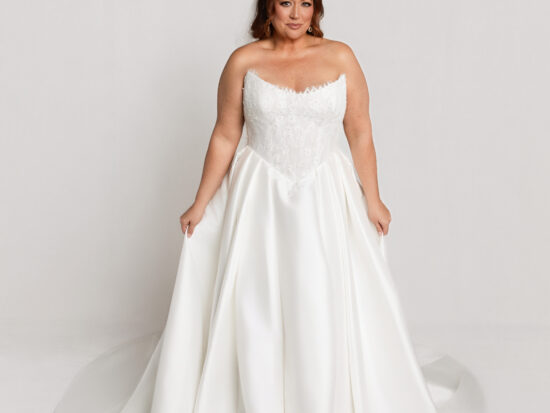 Bride wearing a strapless white wedding gown with a sweetheart neckline and full flowing skirt, standing against a neutral background.